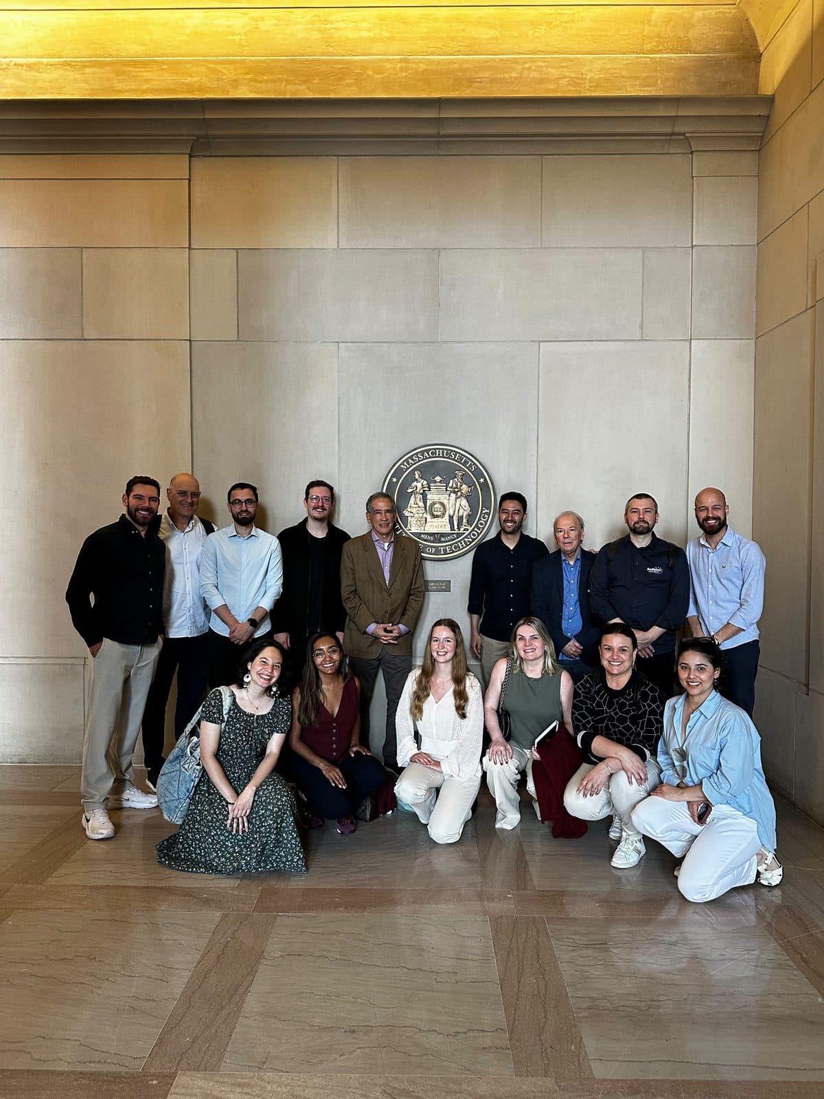Grupo de participantes reunido diante do brasão do MIT